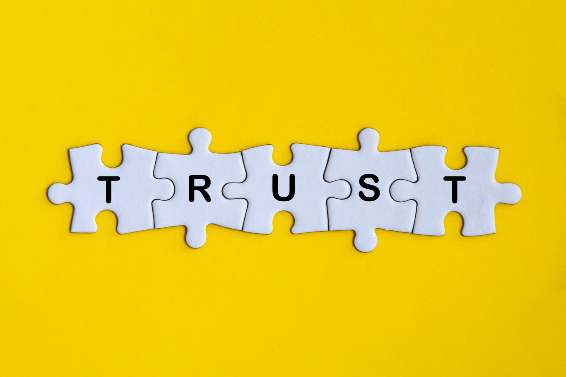 This is a photo of five puzzle pieces that spell out the word "trust. "